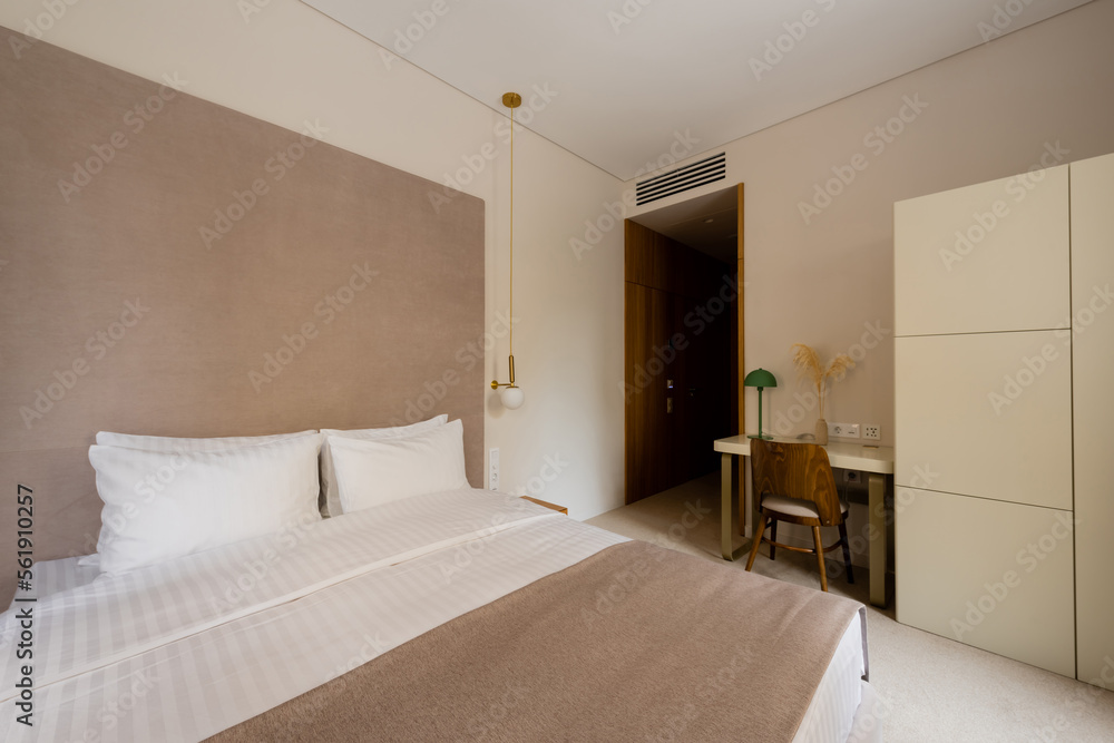 comfortable bed with white bedding near desk and wooden chair in modern hotel bedroom. comfortable bed with white bedding near desk and wooden chair in modern hotel bedroom.