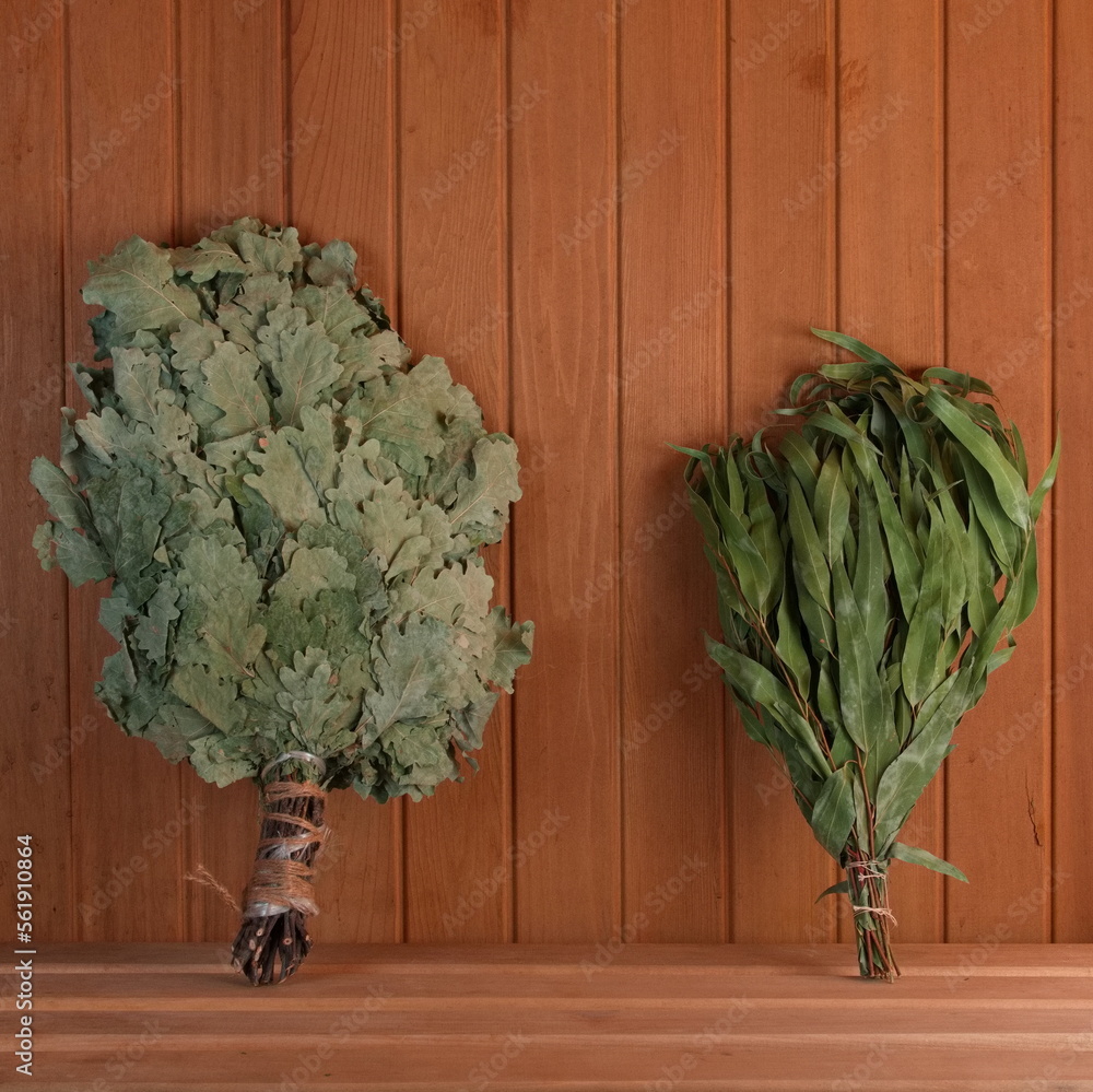 Two dry brooms on a shelf in the sauna. Birch and eucalyptus brooms for the steam room. Square Photo. Wellnes and Aromatherapy - obrazy, fototapety, plakaty 