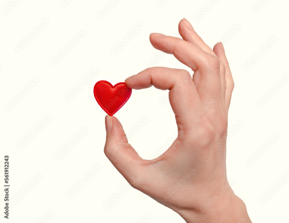 A woman's hand holds a small red heart with her fingers A woman's hand holds a small red heart with her fingers