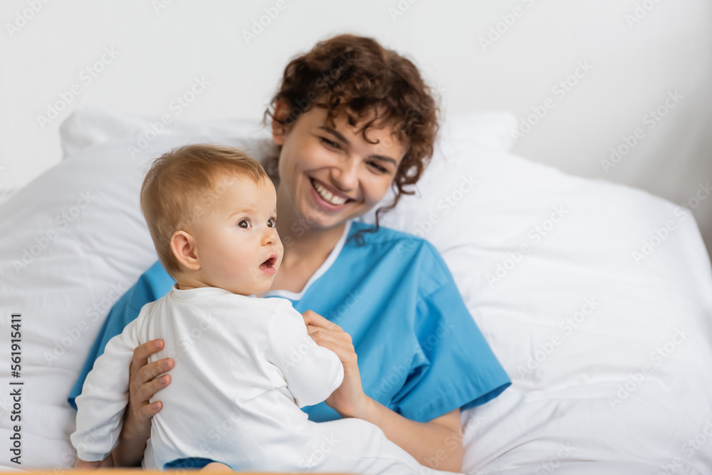 little baby with open mouth looking away near smiling mother in hospital ward. little baby with open mouth looking away near smiling mother in hospital ward.