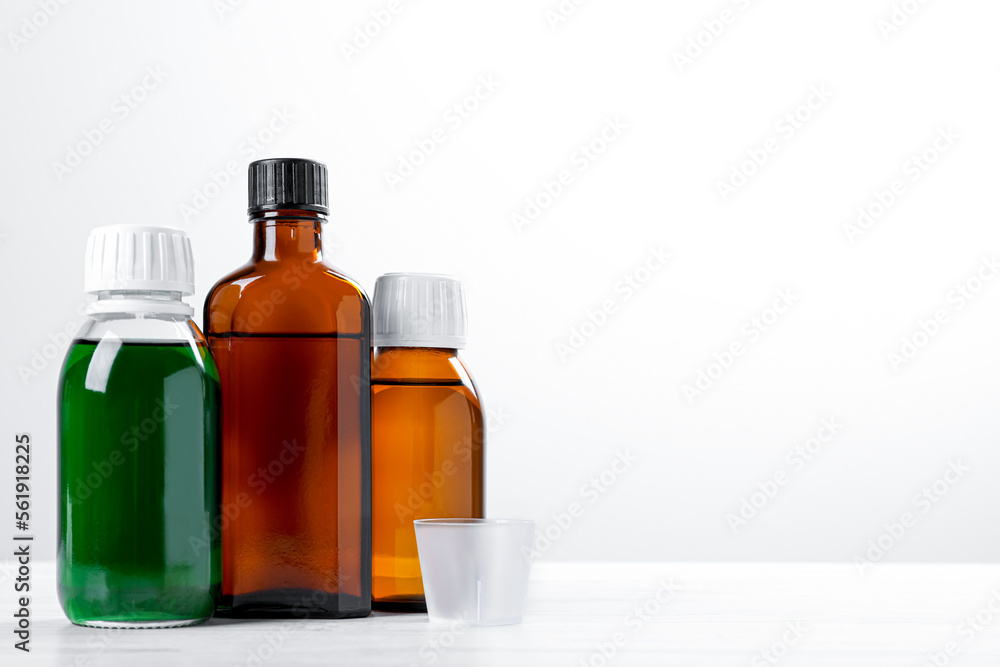 Bottles of syrups with measuring cup on wooden table against white background, space for text. Cough and cold medicine Bottles of syrups with measuring cup on wooden table against white background, space for text. Cough and cold medicine
