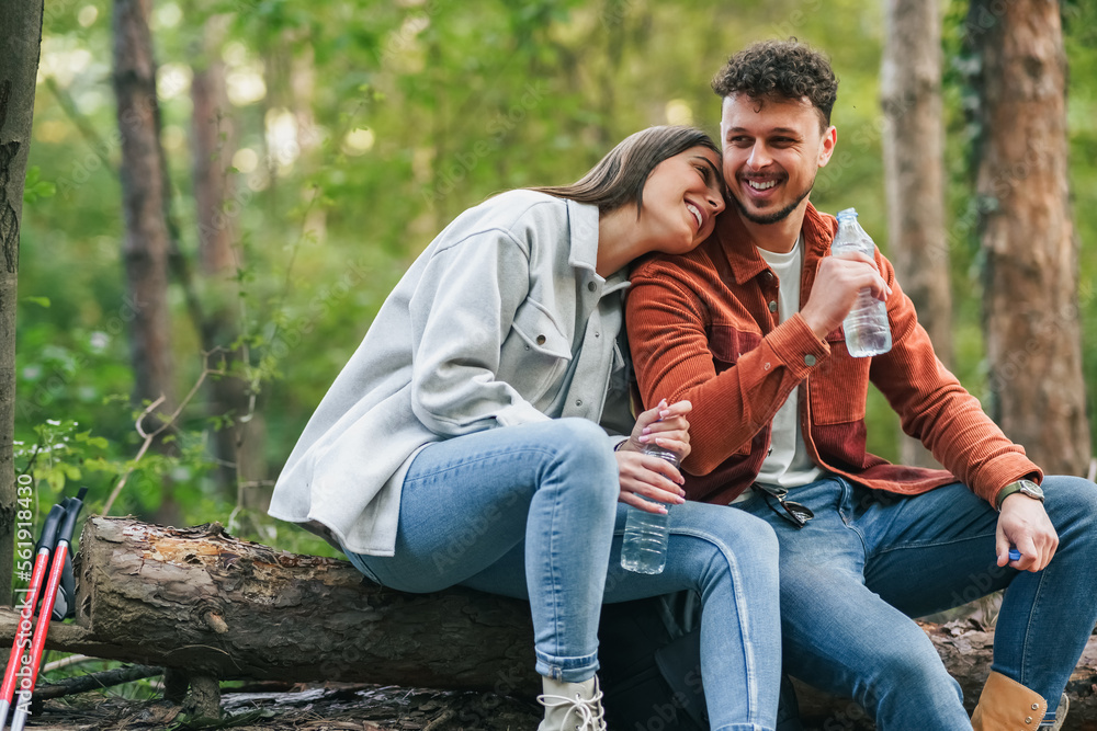 A girl is holding her head on his boyfriend's shoulder and smiling, talking about something witty while sitting at a branch during their nature exploration. A girl is holding her head on his boyfriend's shoulder and smiling, talking about something witty while sitting at a branch during their nature exploration.