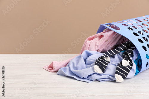 Plastic laundry basket with clothes near beige wall. Space for text