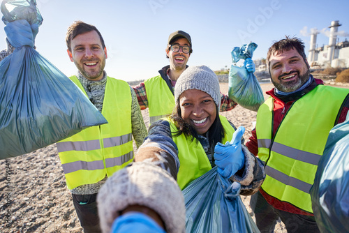 Selfie young activists looking at camera holding a garbage bag trash. People standing with happy expression. Group of cleanup volunteers cleaning up waste in nature. Concept environmental protection.