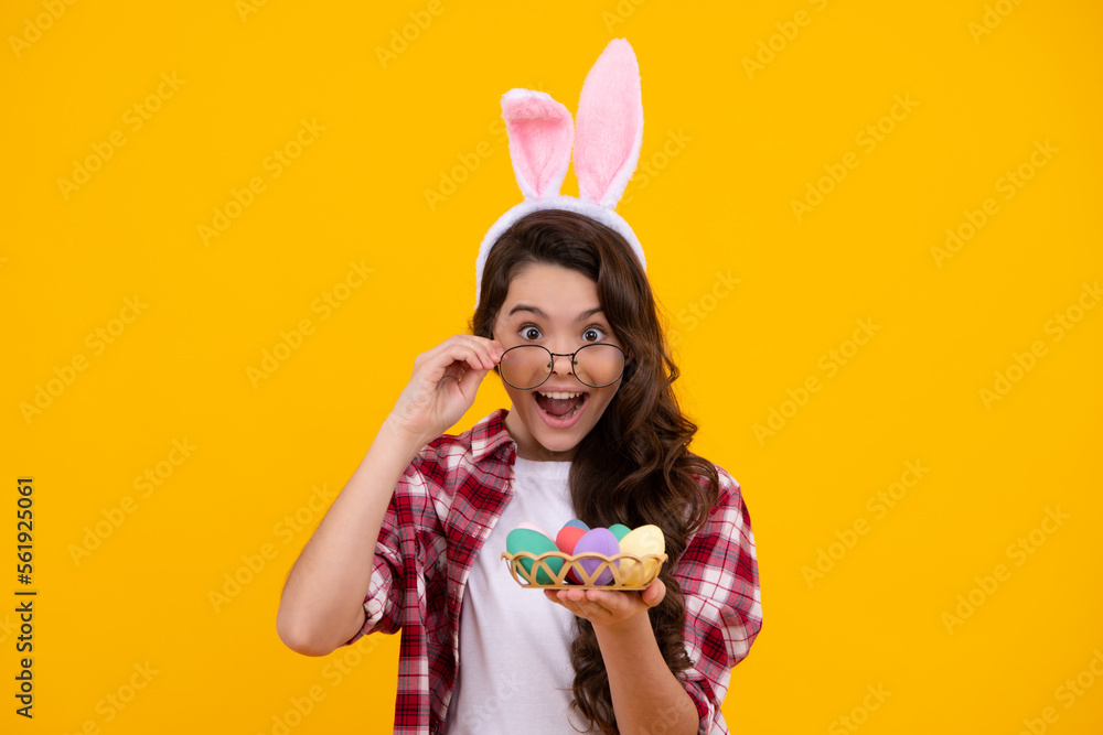 Portrait of teenage girl child wearing bunny ears holding easter eggs isolated at yellow background. Amazed teenager. Excited teen girl.