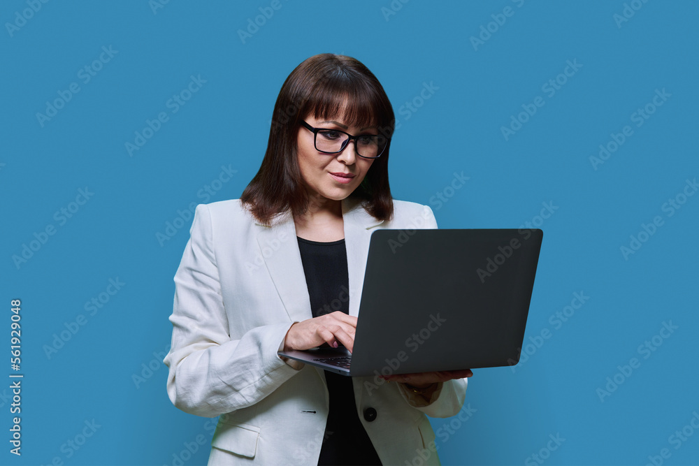 Mature business woman using laptop, on blue studio background Mature business woman using laptop, on blue studio background
