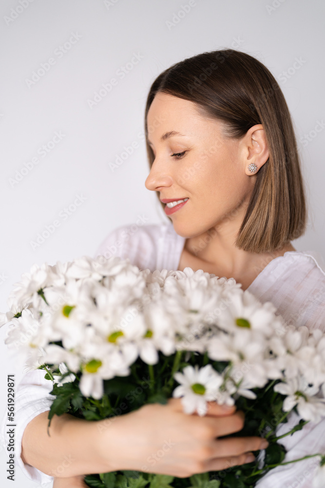 Young beautiful cute sweet lovely smiling woman with hold a bouquet of white fresh flowers on white wall background Young beautiful cute sweet lovely smiling woman with hold a bouquet of white fresh flowers on white wall background