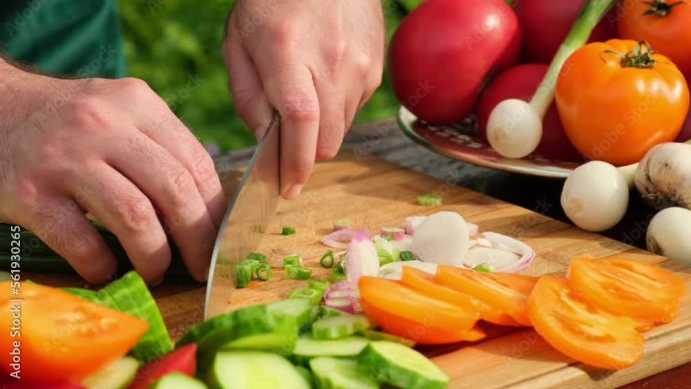 Making vegetable salad outdoors. Cook cuts a salad of tomatoes, cucumbers, greens, onion, olive oil. Healthy meal and nutrition concept. Cooking salad from fresh raw vegetables with knife Making vegetable salad outdoors. Cook cuts a salad of tomatoes, cucumbers, greens, onion, olive oil. Healthy meal and nutrition concept. Cooking salad from fresh raw vegetables with knife