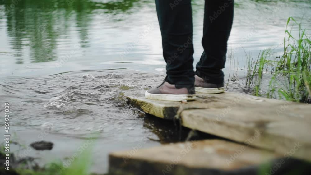 A man stands on the bank of the river on boards going into the water. Close-up shooting A man stands on the bank of the river on boards going into the water. Close-up shooting
