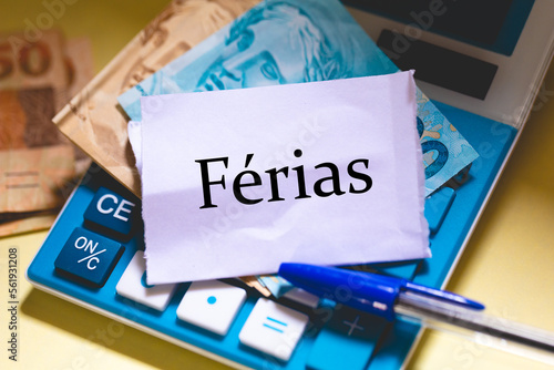 A palavra Férias em Português do Brasil escrita em um pedaço de papel. Notas do Real Brasileiro, uma calculadora e uma caneta na composição. photo