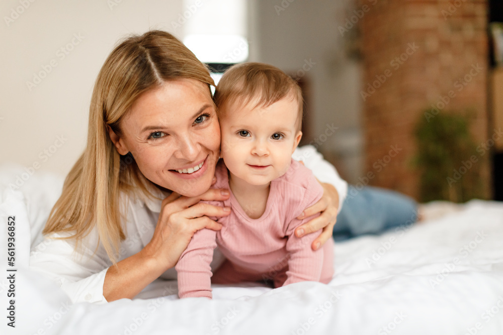 Happy motherhood. Mommy playing with adorable toddler baby crawling on bed, smiling at camera, bedroom interior Happy motherhood. Mommy playing with adorable toddler baby crawling on bed, smiling at camera, bedroom interior