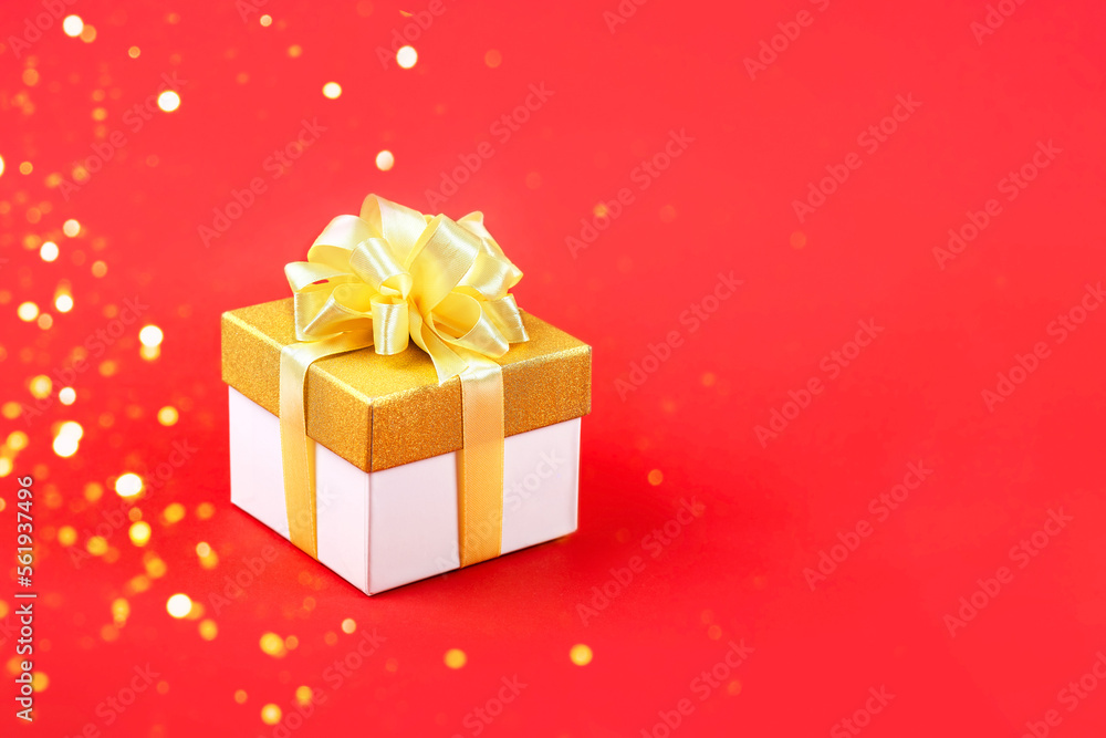 Golden gift box with a satin ribbon bow on red background for a holiday. Happy Valentine's Day, Mother's Day and birthday greeting card.