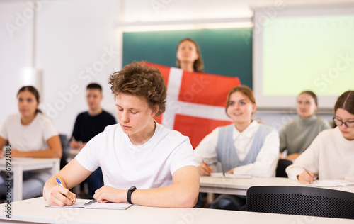 High school teacher tells students about Denmark and holds a Denmark flag in her hands.