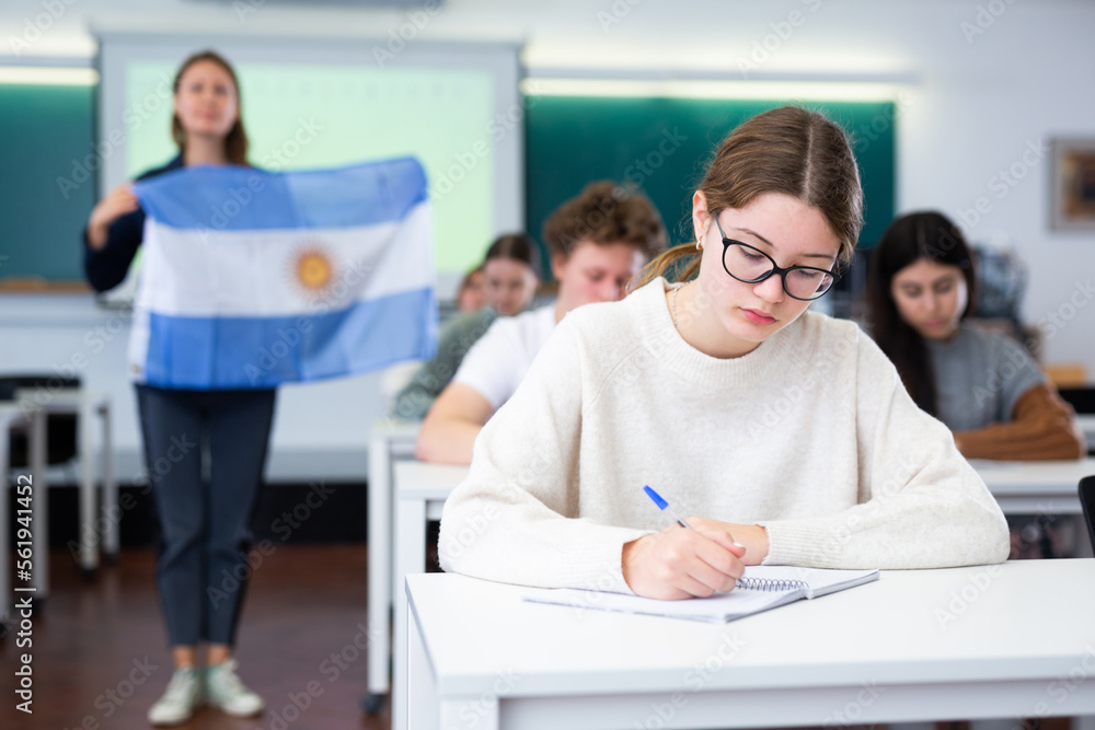 Obraz premium Students study in classroom, teacher stands behind with flag of Argentina