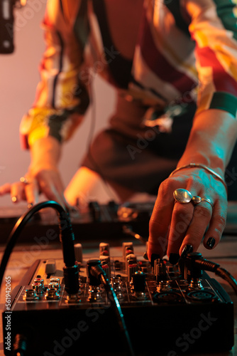 Female performer playing key sounds on mixing turntables, using audio dj equipment and stereo instrument to play techno music. Enjoying melody mix at nightclub, stage party in studio. photo