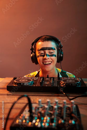 Young performer looking at dj turntables in studio, preparing to mix techno music and have fun at nightclub. Woman with crazy make up watching mixer on table, look closely and acting silly. photo