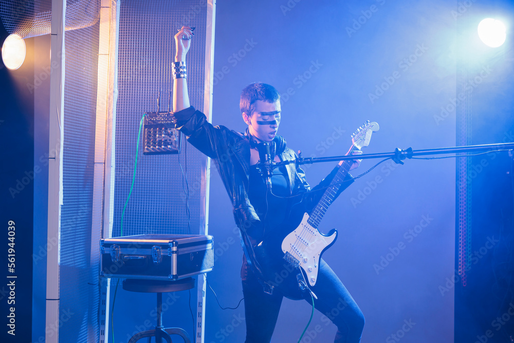 Fototapeta premium Crazy artist performing live show in studio, playing electric guitar and singing heavy metal music. Cool funky singer doing alternative rock performance with leather jacket and dark make up.