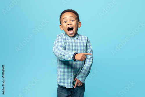 Amazed kid boy showing shocking advertisement, pointing at copy space for text or advertisement over blue background