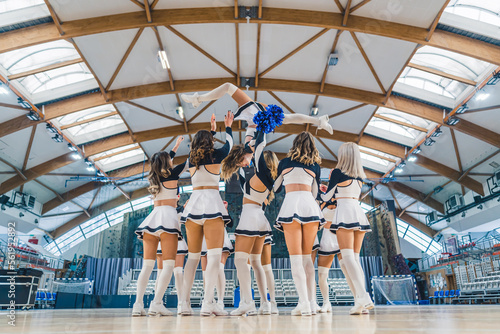 Group of cheerleaders standing in a circle with one doing a flip in the air. Sport concept. High quality photo