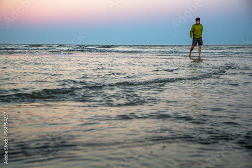 St Simons Island, Georgia, USA. A man in shorts and a jacket walks through shallow water under a lavender sunset sky. photo