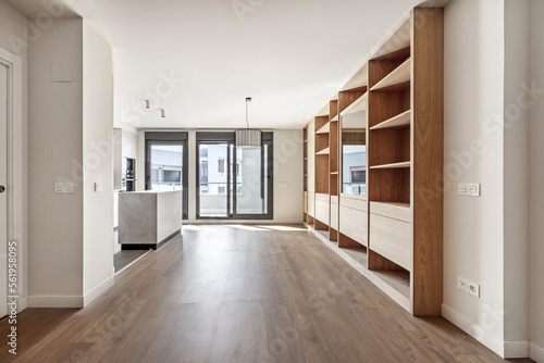 Living room of an empty house with custom-made oak bookcase  open kitchen on one side and terrace with access to a terrace with sliding doors