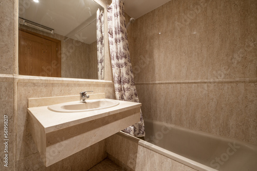 Tiled bathroom in cream marble with built-in mirror  marble borders and toilets and porcelain tub with curtains