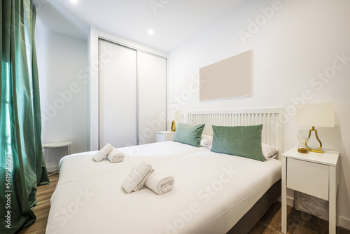 Bedroom with a white wooden double bed with a barred headboard  a built-in wardrobe with sliding doors and white bedside tables