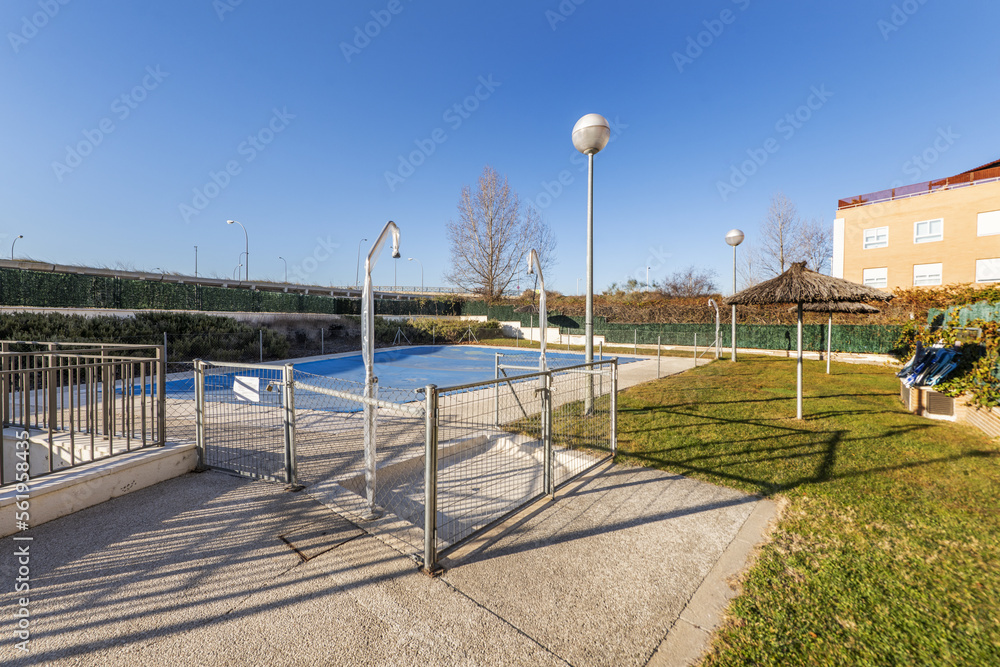 A summer pool in a garden with parasols and railings covered with a tarpaulin to spend the winter
