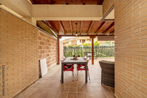 Patio of a detached house with light brown stoneware floors, exposed brick walls, lawned gardens and a porch made of varnished pine logs photo