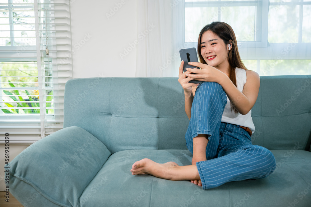 Social media networks. Happy beautiful female relax and shopping online with smartphone, Smiling Asian woman sitting on sofa reading news on mobile smart phone at living room at home Social media networks. Happy beautiful female relax and shopping online with smartphone, Smiling Asian woman sitting on sofa reading news on mobile smart phone at living room at home