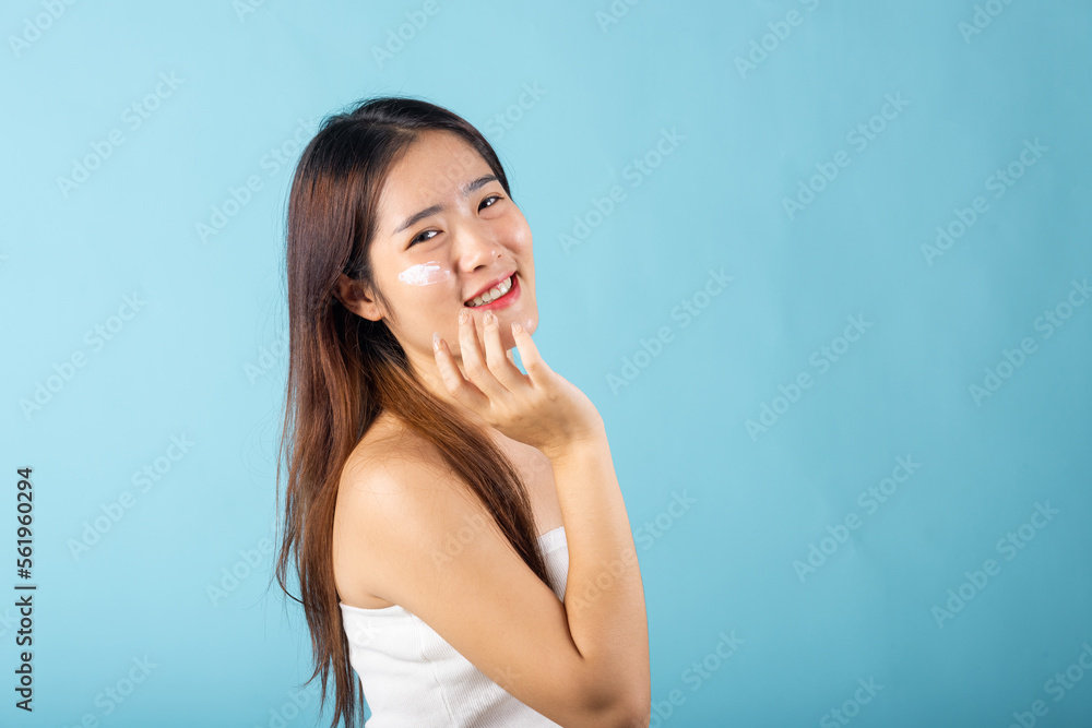 Skin care and beauty concept. young woman applying moisturizer cream on her face studio shot isolated on blue background, Happy beauty portrait female gets cream on her cheek, health clean skin Skin care and beauty concept. young woman applying moisturizer cream on her face studio shot isolated on blue background, Happy beauty portrait female gets cream on her cheek, health clean skin