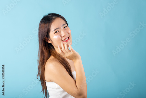 Skin care and beauty concept. young woman applying moisturizer cream on her face studio shot isolated on blue background, Happy beauty portrait female gets cream on her cheek, health clean skin