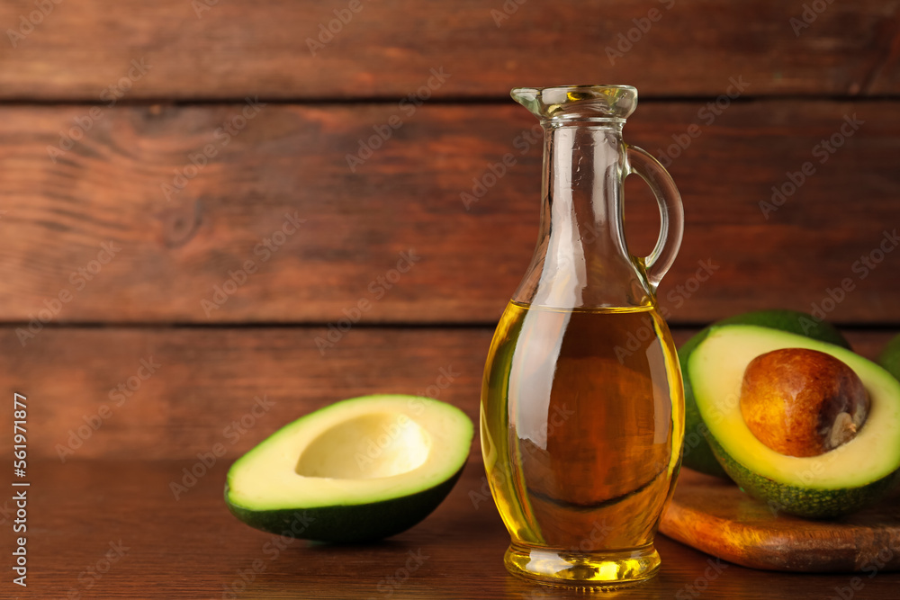 Glass jug of cooking oil and fresh avocados on wooden table, space for text Glass jug of cooking oil and fresh avocados on wooden table, space for text