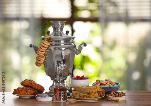 Traditional Russian samovar and treats on wooden table against window in room