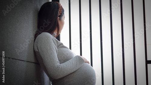 Portrait of mature pregnant woman at home looking outside the fence. Young pregnant woman standing by fence at home and thinking about the future