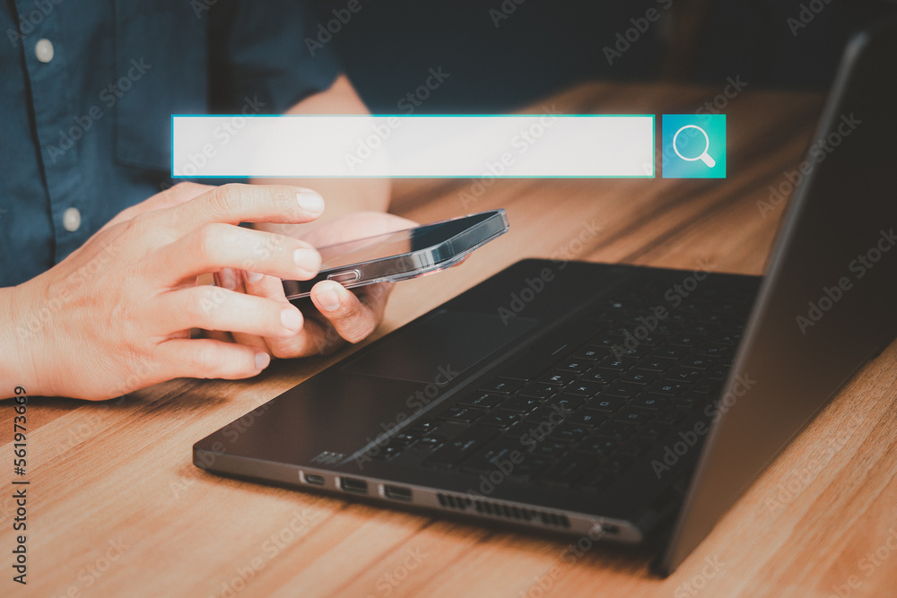 Adult man hand working with a mobile phone and computer laptop on the desk. Searching browsing internet data information with blank search bar. Search Engine Optimization SEO networking concept. Adult man hand working with a mobile phone and computer laptop on the desk. Searching browsing internet data information with blank search bar. Search Engine Optimization SEO networking concept.