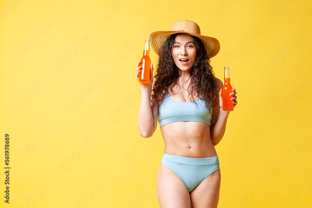 young curly brunette girl in a blue swimsuit in summer holds two bottles with an orange drink and smiles young curly brunette girl in a blue swimsuit in summer holds two bottles with an orange drink and smiles