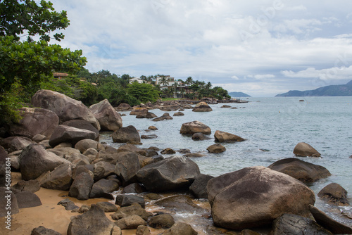 Pedras na Praia Grande - ILHABELA, SP, BRAZIL - NOVEMBER 29, 2022: Rocks on the left side of Praia Grande with houses by the sea in the background. photo