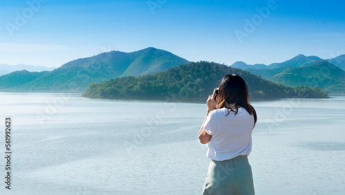 Young asia girl with her back turned taking a photo with her digital camera to papagayo beach on islands emerging from the surface. Travelers lifestyle and natural in Kaeng Krachan Thailand. photo
