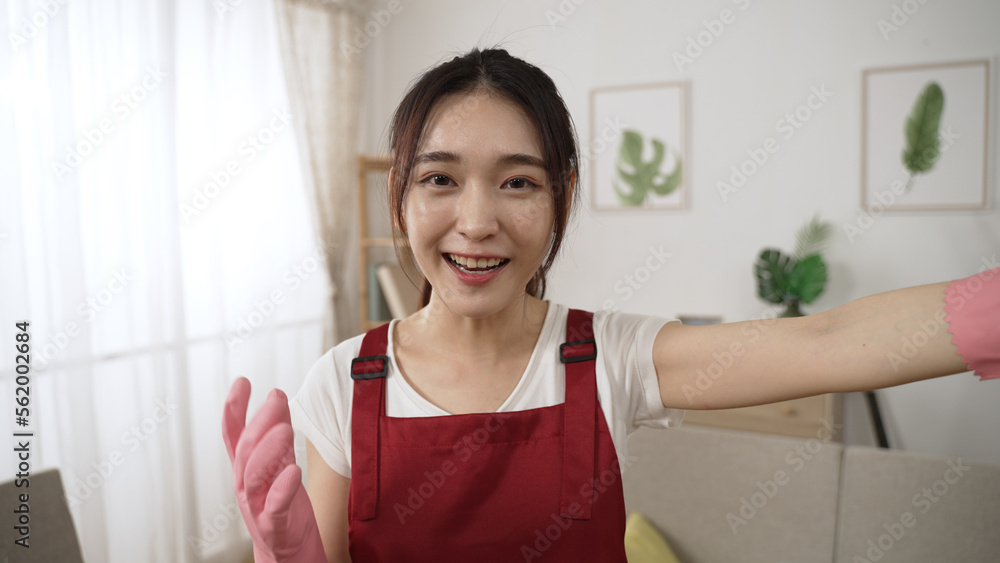cheerful asian female influencer in rubber gloves is waving hi to mobile came and gesturing backward while live streaming about cleaning and organizing at home cheerful asian female influencer in rubber gloves is waving hi to mobile came and gesturing backward while live streaming about cleaning and organizing at home