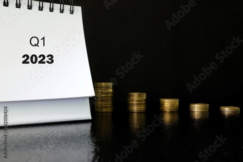 First quarter of 2023 negative performance financial report and fiscal concept. Downward arrow with decreasing coins and calendar in black background. photo