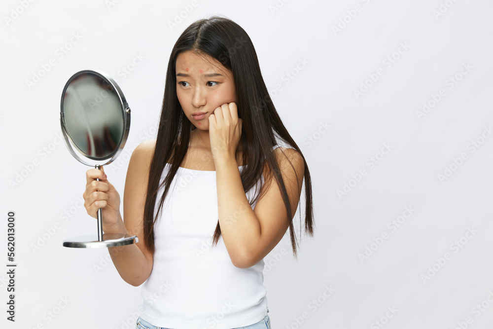 Asian woman with mirror in hand facial skin problems, acne and inflammation, red rash and allergies, chicken pox, sadness from rashes. Facial skin care concept for diseases and nerves Asian woman with mirror in hand facial skin problems, acne and inflammation, red rash and allergies, chicken pox, sadness from rashes. Facial skin care concept for diseases and nerves
