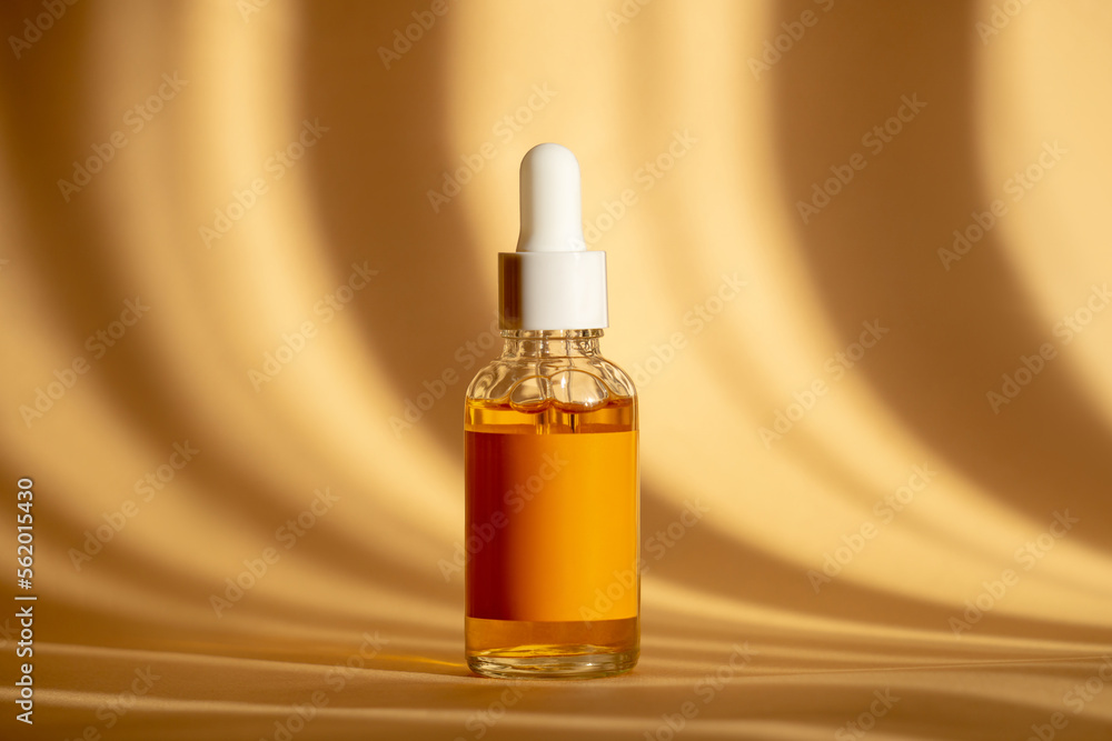 Naklejka premium Glass bottle with white dropper lid with serum on brown background in sunlight. Orange essence in transparent unmarked container. Mockup of cosmetic product for skin care