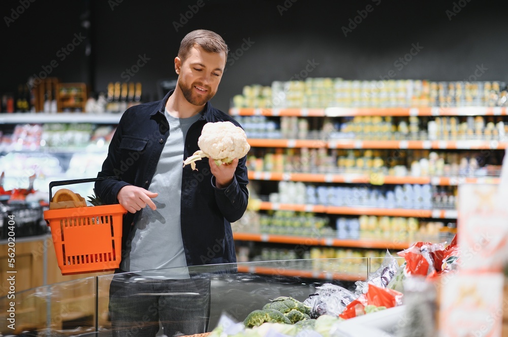 Young man buying groceries at the supermarket. Other customers in background. Consumerism concept.