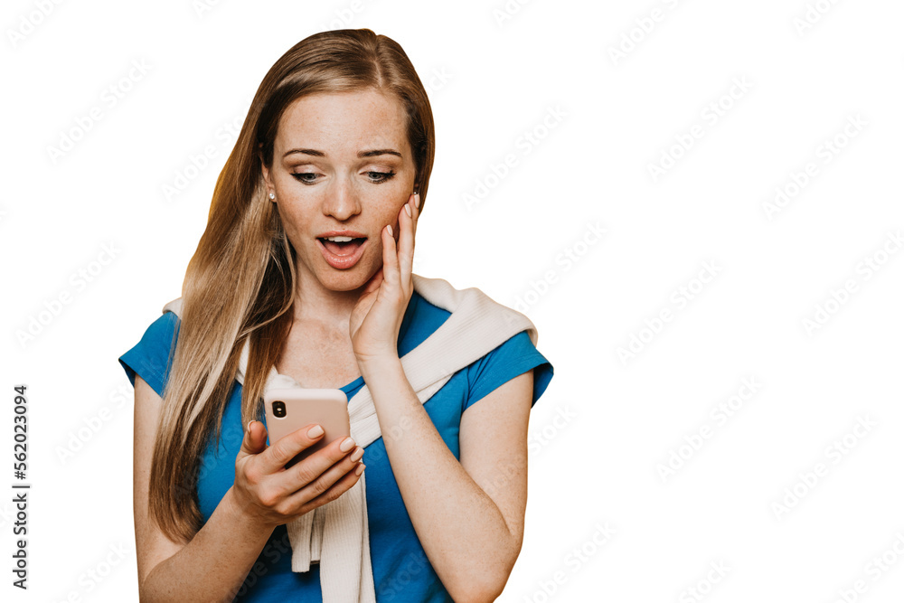 Discouraged ginger American young woman in blue t-shirt in sweatshirt tied neck holds phone looks at screen in surprise with opened mouth touches cheek excited against transparent background, message. Discouraged ginger American young woman in blue t-shirt in sweatshirt tied neck holds phone looks at screen in surprise with opened mouth touches cheek excited against transparent background, message.
