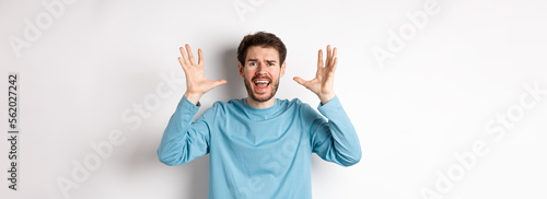 Image of freaked out young man screaming and shaking hands, shouting at camera frustrated or worried, panicking over white background photo