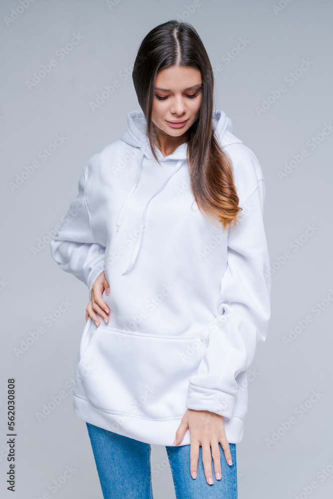Young woman in white sweatshirt, mockup for logo or branding design posing in studio on light background. Caucasian girl with long hair in cozy clothes Young woman in white sweatshirt, mockup for logo or branding design posing in studio on light background. Caucasian girl with long hair in cozy clothes