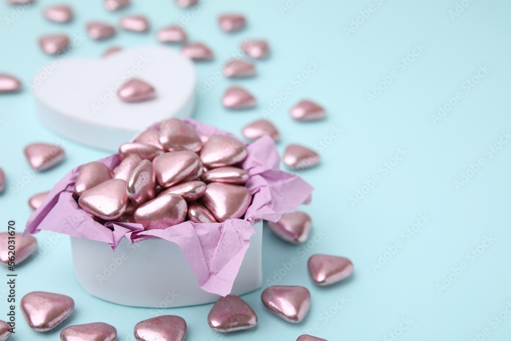 Box and delicious heart shaped candies on light blue background. Space for text