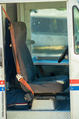 Mail delivery truck with red and blue stipes on white van with brown seat and visible seatbelt to deliver mail to mailboxes