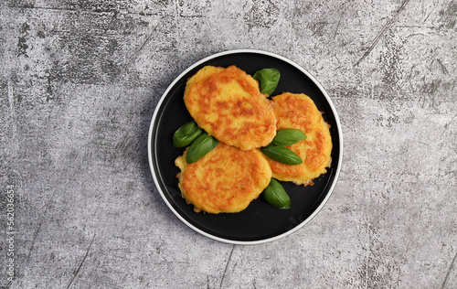 Potato fritters with basil leaves on a round plate on a dark gray background. Top view, flat lay